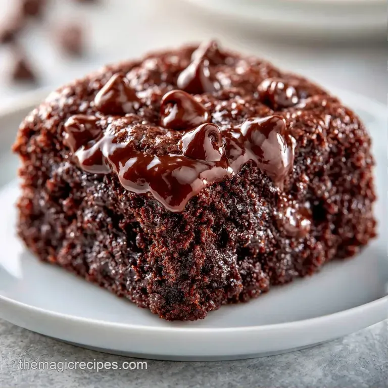 A slice of moist chocolate cake with melted chips, served on a white plate with a dusting of powdered sugar.